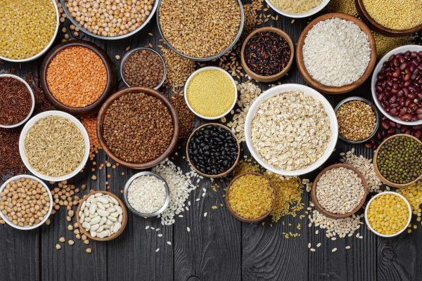 Different cereals, grains, seeds, groats, legumes and beans in bowls, top view of raw porridge collection on black wooden background with copy space